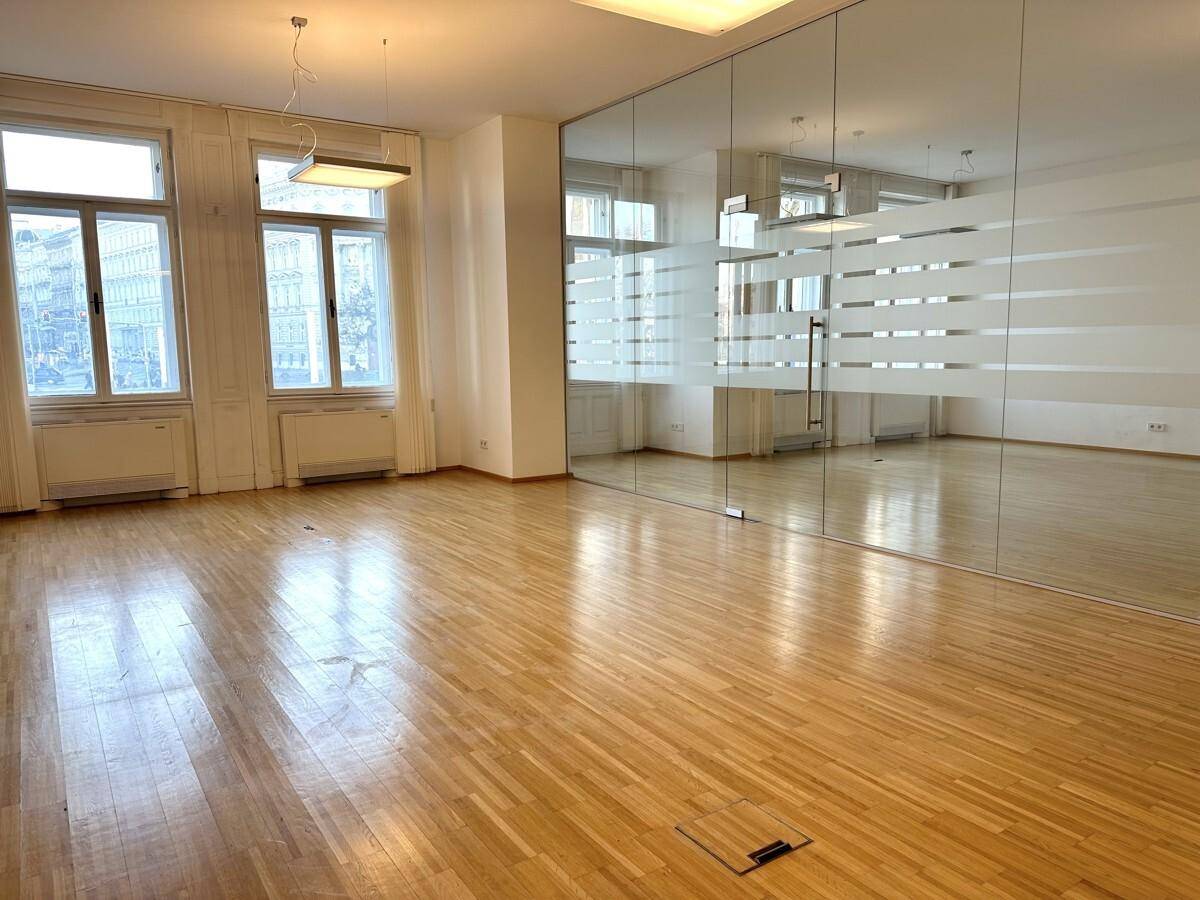 Geräumiger Büroraum mit Holzboden, großen Fenstern und einer modernen Glaswand.