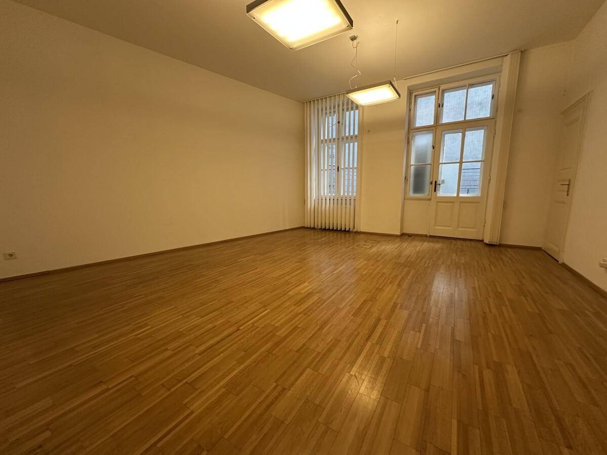 Heller Büroraum mit Holzboden, hohen Fenstern und weiß gestrichenen Wänden.