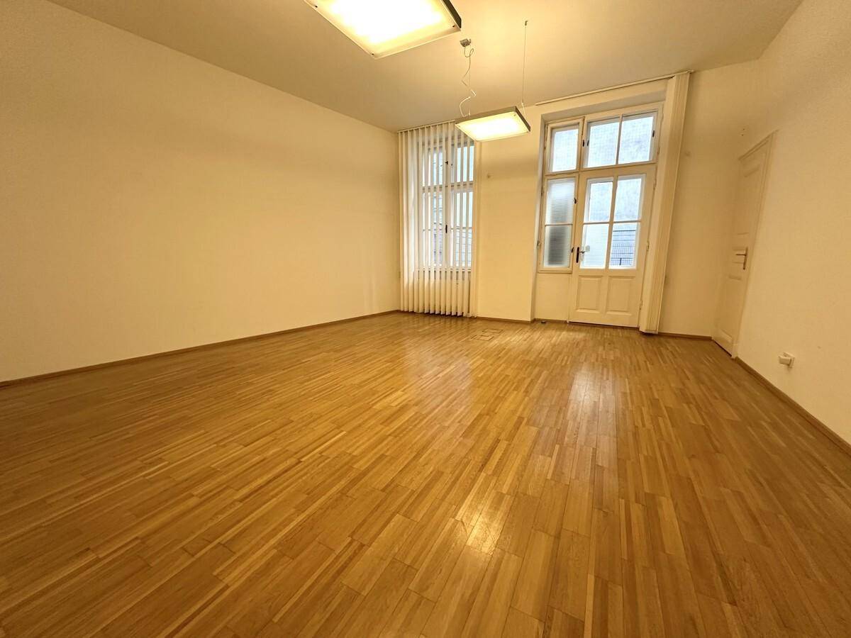 Heller Büroraum mit Holzboden, hohen Fenstern und weiß gestrichenen Wänden.