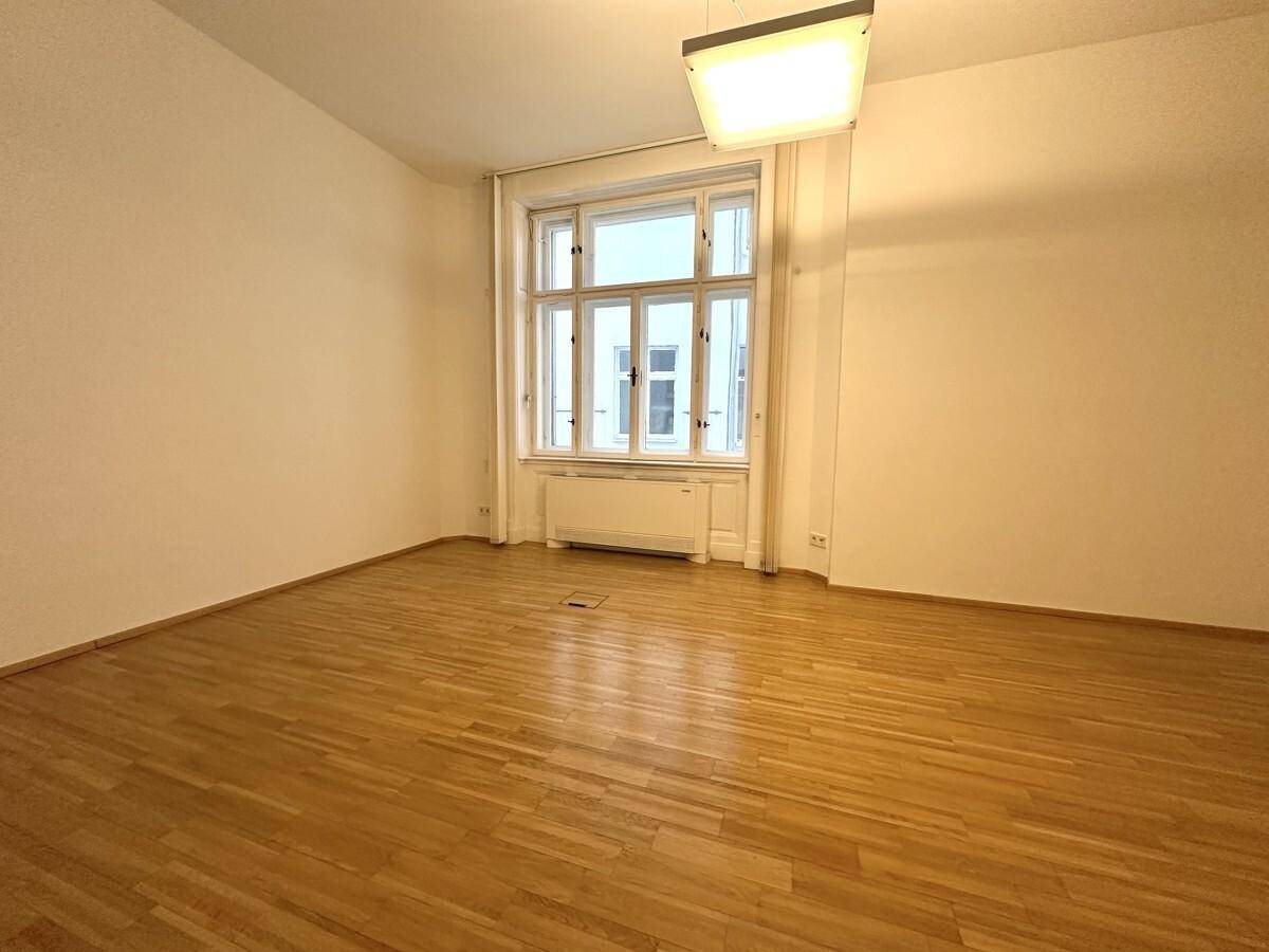 Heller Büroraum mit Holzboden, einem großen Fenster und weiß gestrichenen Wänden.