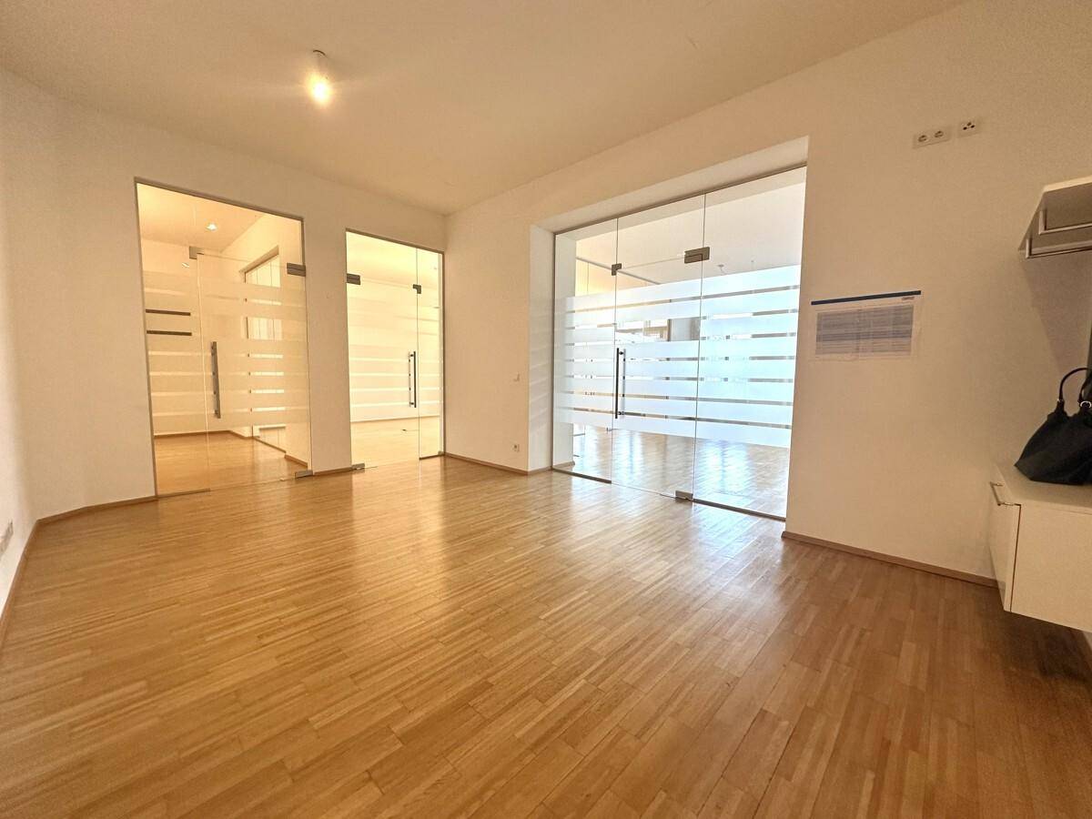 Großer Bürobereich mit Holzboden und mehreren modernen Glasabtrennungen zu weiteren Räumen.