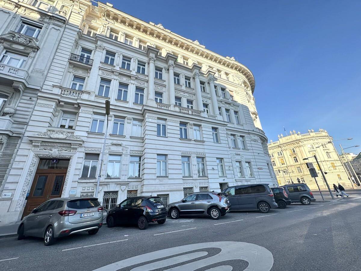 Historisches Gebäude mit klassischer Architektur und geparkten Autos an einer Stadtstraße.