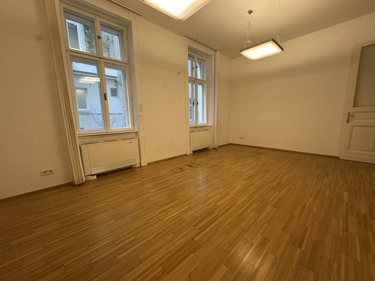 Heller Büroraum mit Holzboden, hohen Fenstern und weiß gestrichenen Wänden.