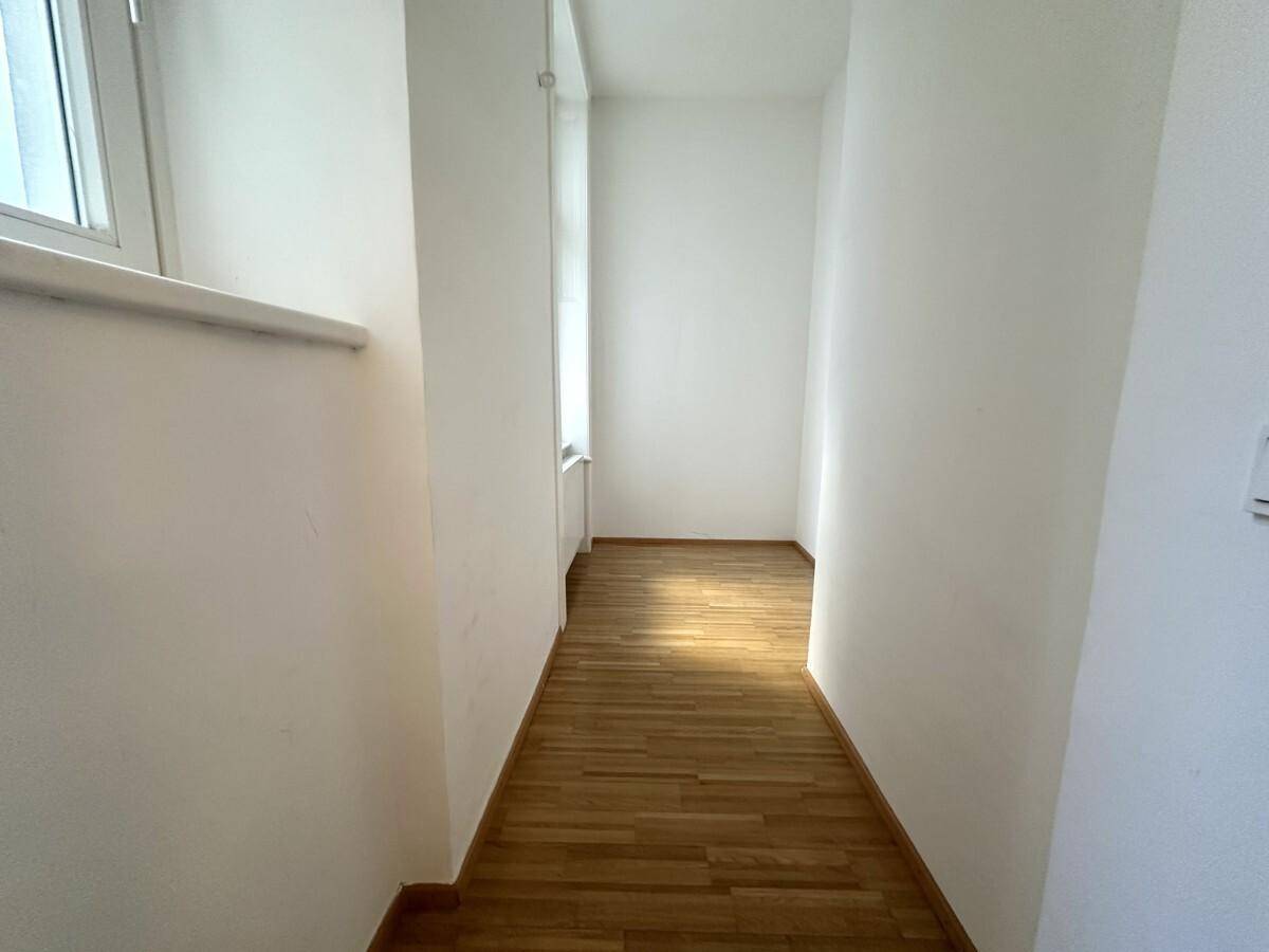 Heller Büroraum mit Holzboden, einem großen Fenster und weiß gestrichenen Wänden.