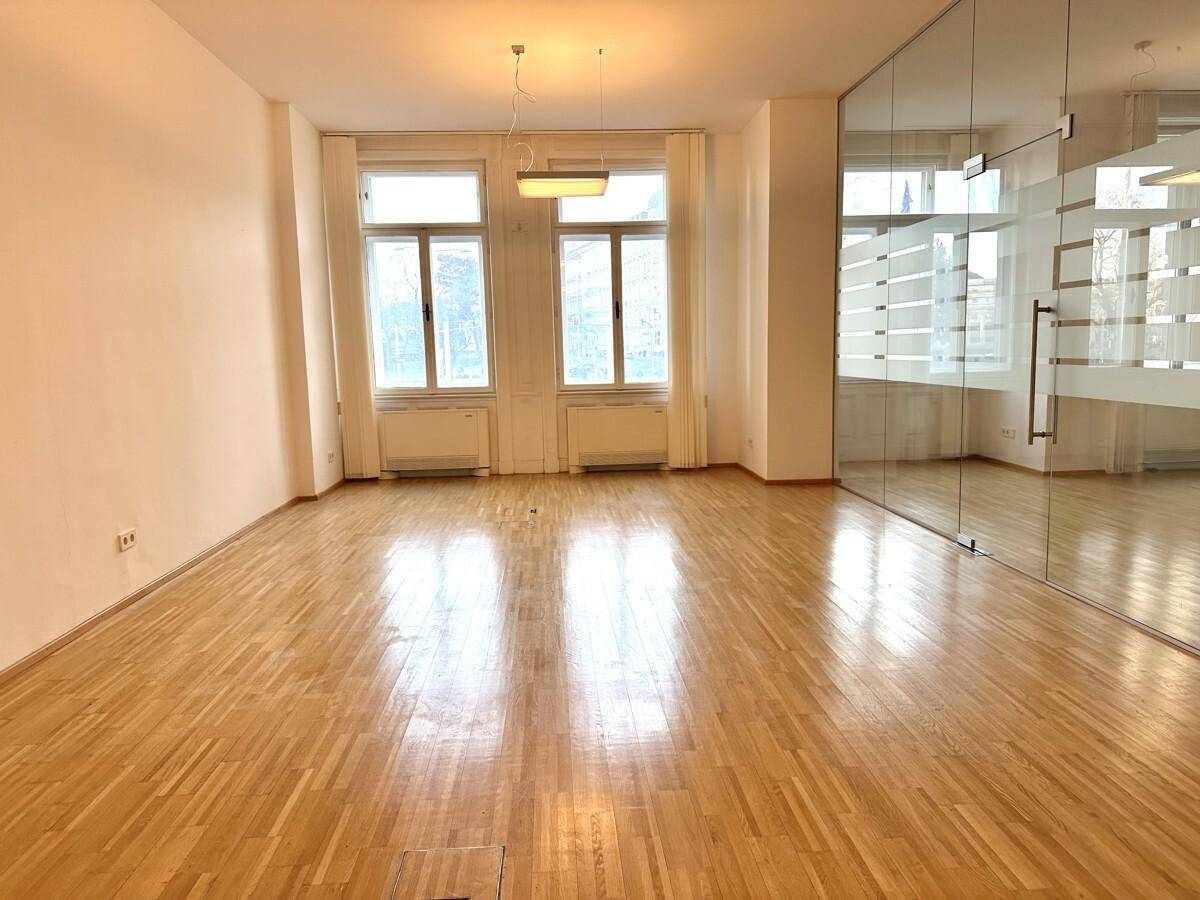 Heller Büroraum mit Holzboden, einem großen Fenster und weiß gestrichenen Wänden.
