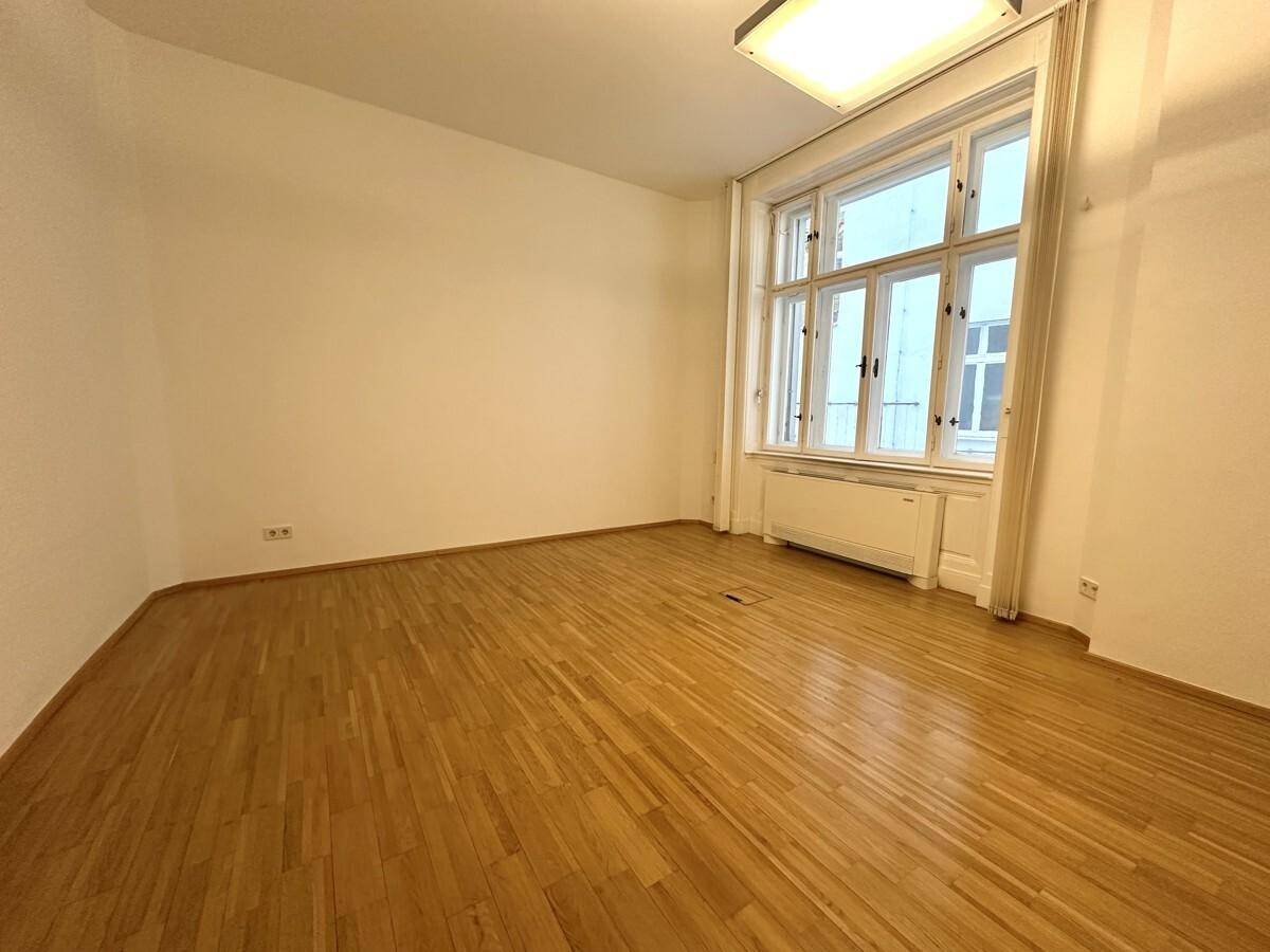 Leerer Raum mit hohen Fenstern und glänzendem Holzboden, ideal für verschiedene Nutzungsmöglichkeiten.