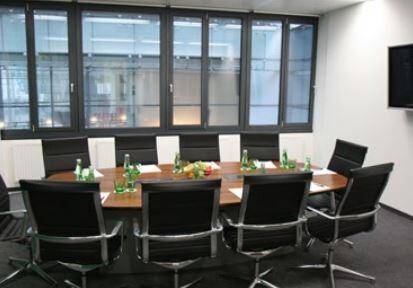 Eleganter Konferenzraum mit ovalem Holztisch, bequemen schwarzen Stühlen und großen Fenstern.