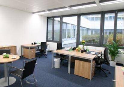 Helles und modernes Büro mit mehreren Arbeitsplätzen, großen Fenstern und blauem Teppichboden.