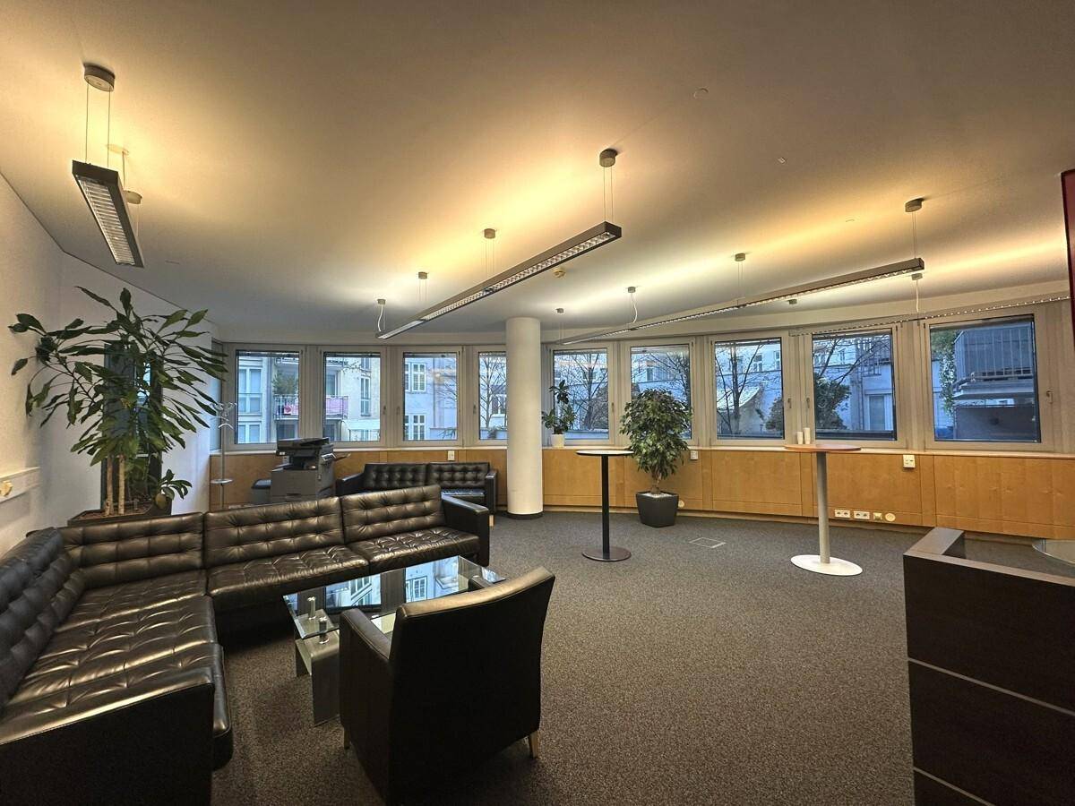 Gemütlicher Loungebereich mit schwarzen Ledersofas, Couchtischen und Pflanzen, ideal für Pausen und informelle Treffen.