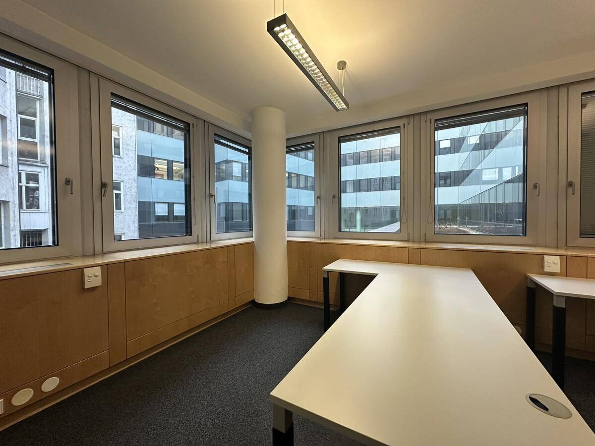 Helles Bürozimmer mit mehreren Fenstern, einem zentralen Pfeiler und modernen Schreibtischen, ideal für konzentriertes Arbeiten.