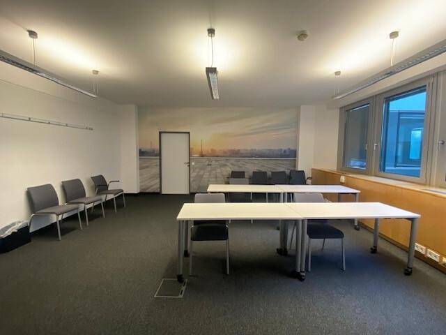 Moderner Besprechungsraum mit flexiblen Tischen und Stühlen, akzentuiert durch eine große Wandtapete mit Landschaftsmotiv.