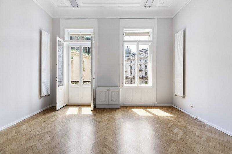 Großer, heller Raum mit Fischgrätparkett, hohen Decken und zwei Fenstern im Obergeschoss.