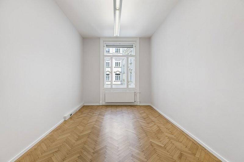 Schmaler Raum mit Fischgrätparkett, hohen Decken und einem großen Fenster im Obergeschoss.