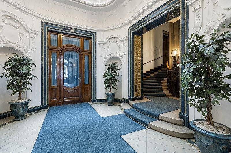 Eleganter Eingangsbereich mit Holztür, Pflanzen und Zugang zu einer Treppe in einem historischen Gebäude.