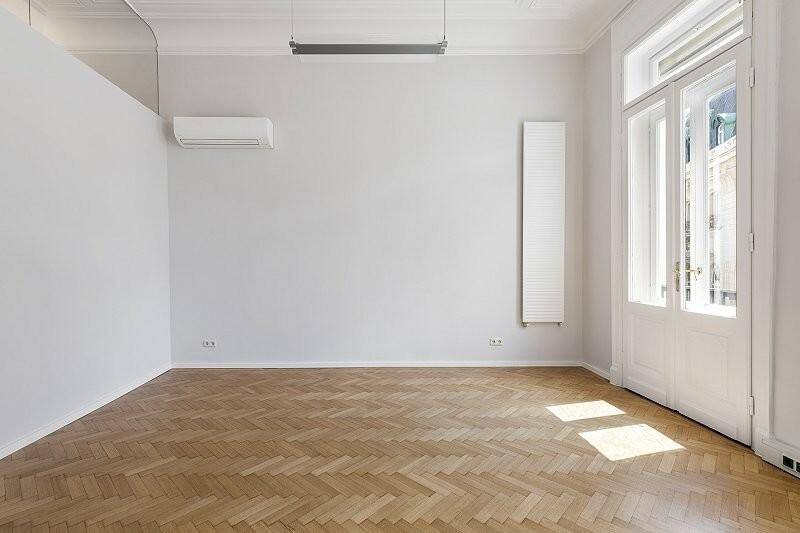 Geräumiger Raum mit Fischgrätparkett, hohen Decken, Klimaanlage und Fenster im Obergeschoss.
