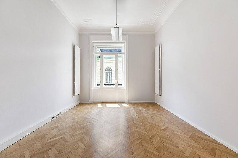 Heller, leerer Raum mit Fischgrätparkett, hohen Decken und einem Fenster im Obergeschoss.