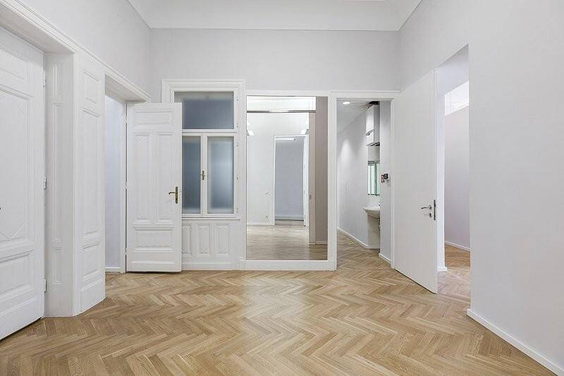 Heller Raum mit Fischgrätparkett, hohen Decken und mehreren Türen in einem renovierten Altbau.