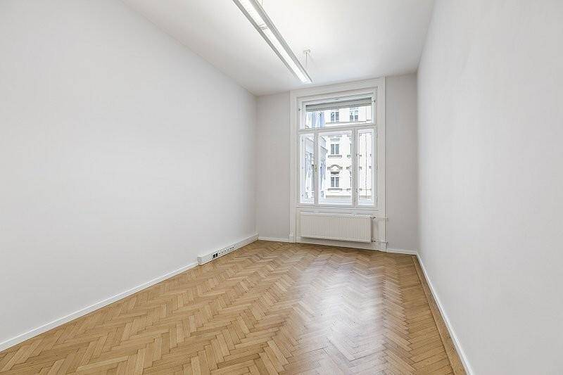 Heller Raum mit Fischgrätparkett, hohen Decken und einem großen Fenster im Obergeschoss.