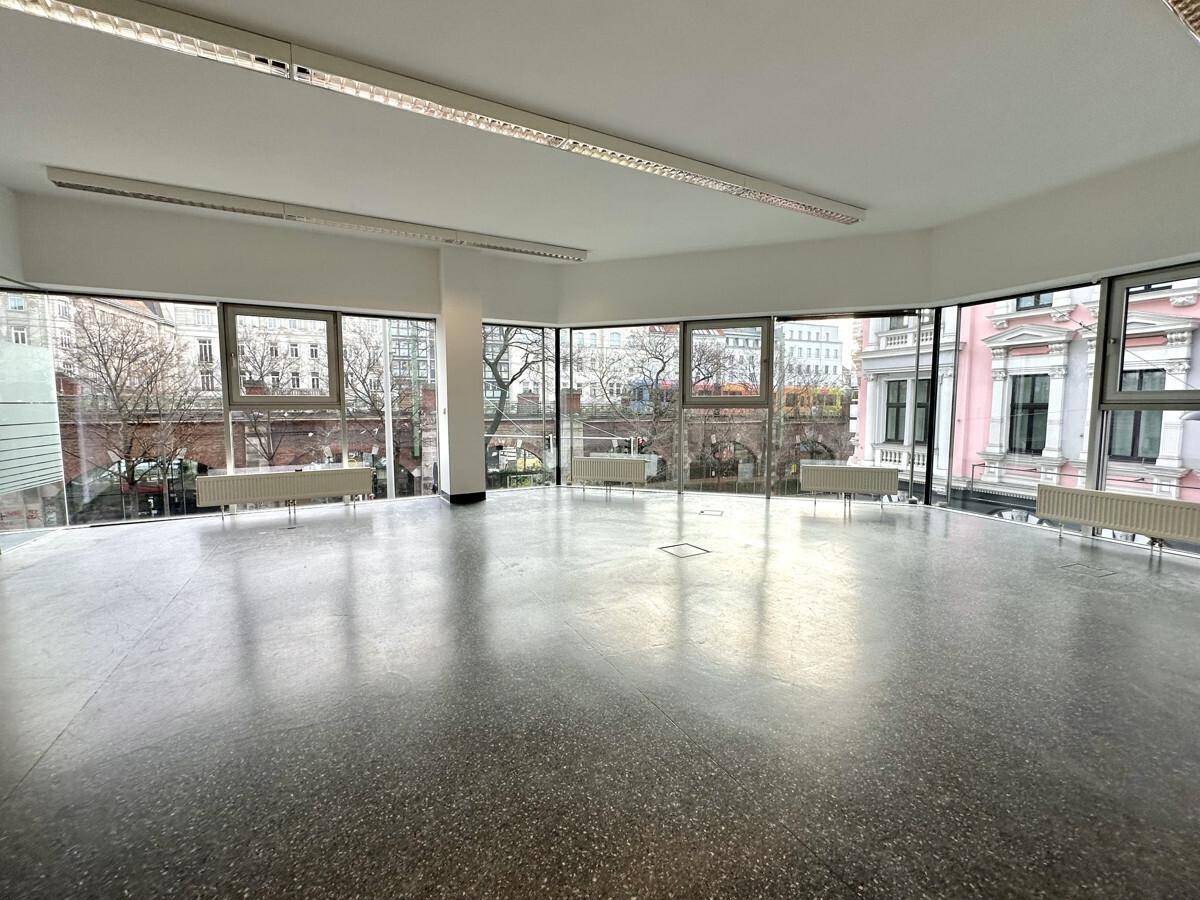 Geräumiger, leerer Büroraum mit großen Fenstern, viel Tageslicht und Blick auf die Stadt.