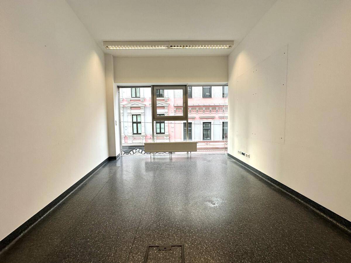 Kleiner, leerer Büroraum mit Fensterfront, Blick auf die Stadt und dunklem Fliesenboden.