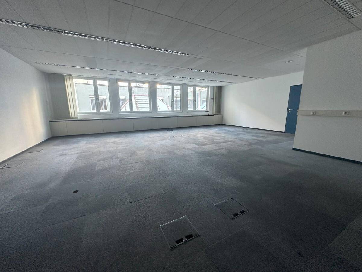 Großes, leeres Büro mit Teppichboden und einer Reihe von Fenstern, die Tageslicht hereinlassen.