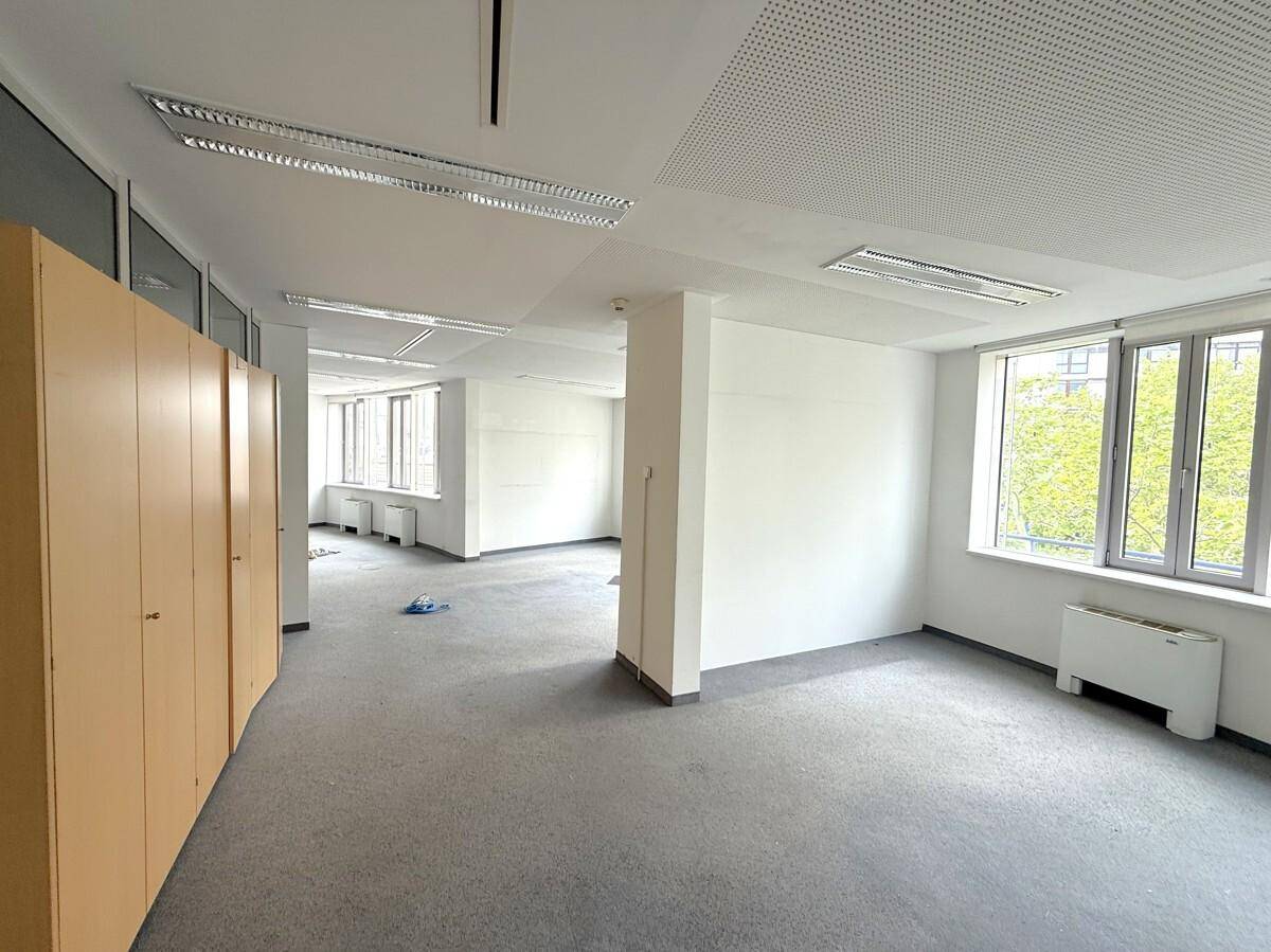 Großer offener Bürobereich mit grauem Teppichboden, weißen Wänden und praktischen Holzschränken.