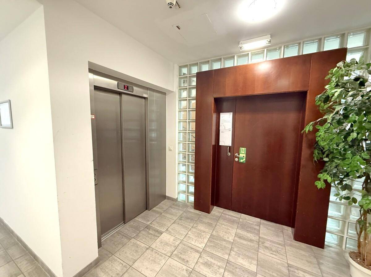Heller Flur mit modernem Aufzug und einer Holztür, ergänzt durch eine Glasbausteinwand.