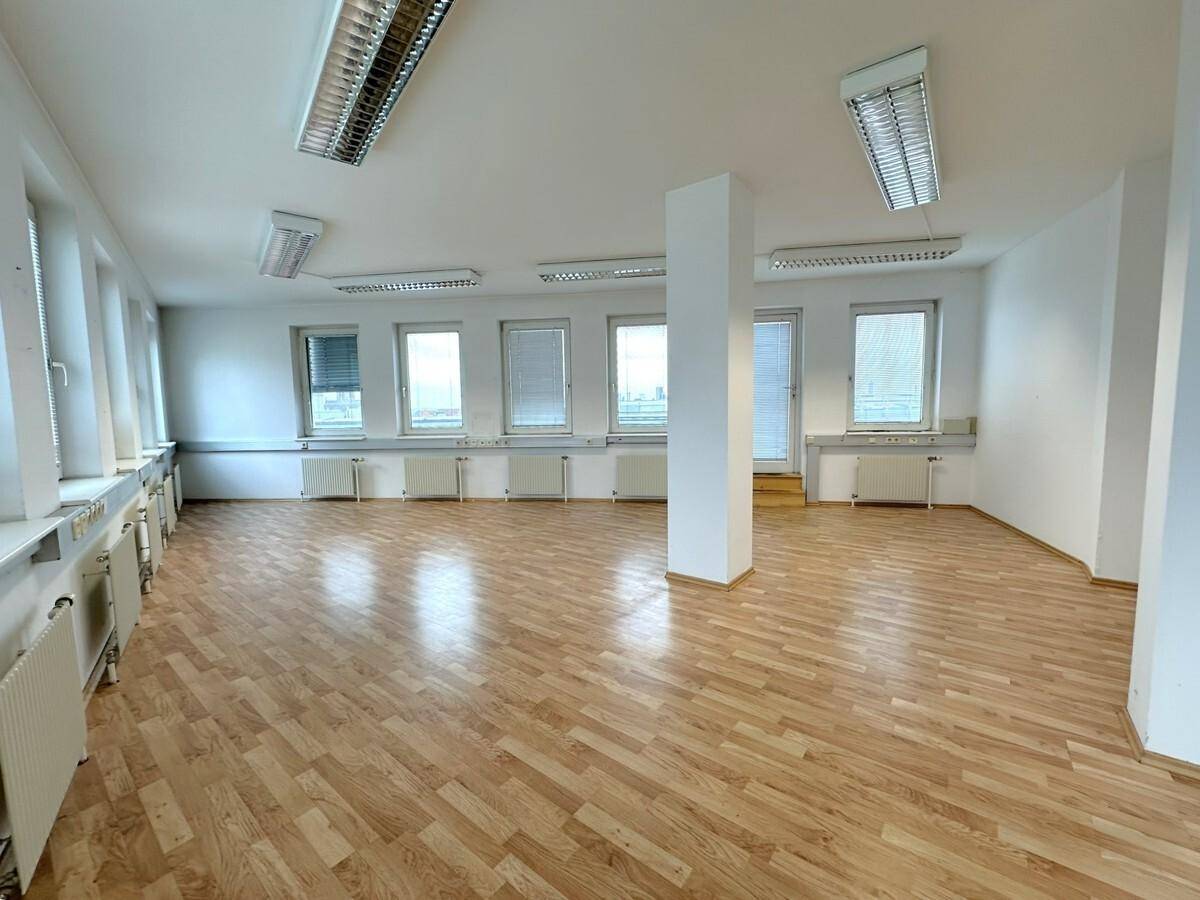 Helles und geräumiges Büro mit Laminatboden, vielen Fenstern und guter Beleuchtung, ideal für verschiedene Nutzungen.