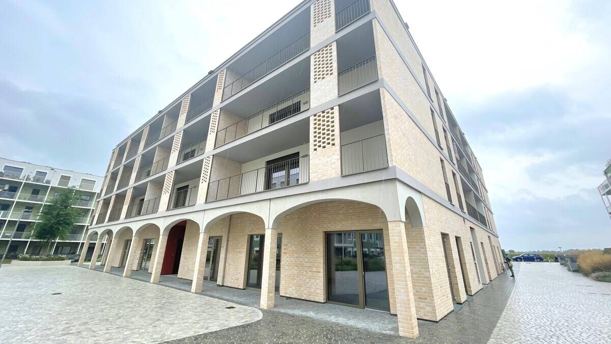 Weitwinkelansicht eines modernen Wohngebäudes mit mehreren Balkonen und Arkaden im Erdgeschoss.