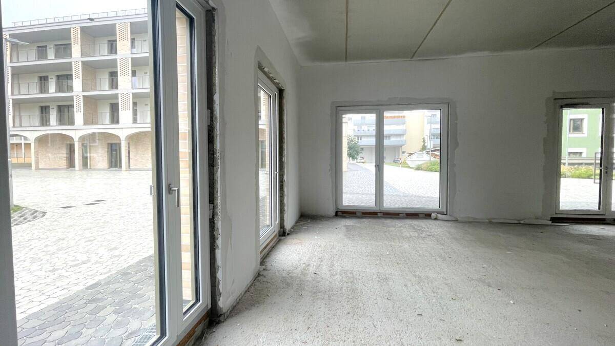 Innenansicht eines Gewerberaums mit großen Fenstern, die den Blick auf den Außenbereich freigeben.