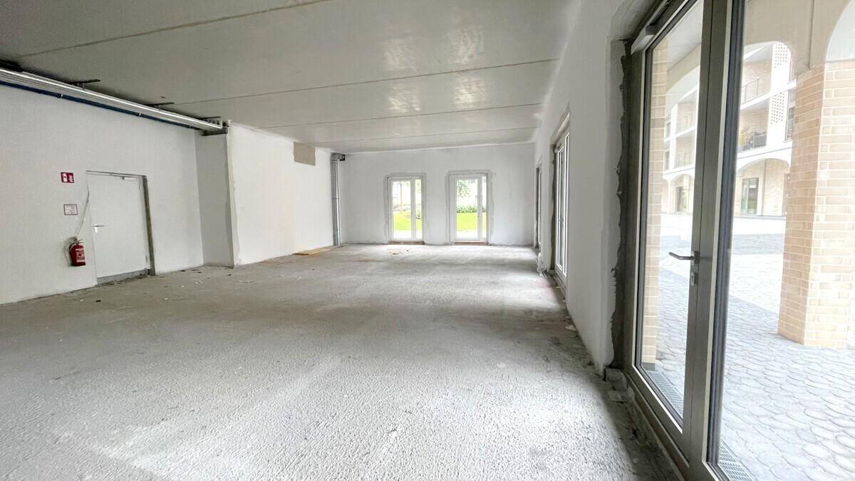 Heller Gewerberaum im Erdgeschoss mit großen Fenstern und Blick auf den gepflasterten Außenbereich.