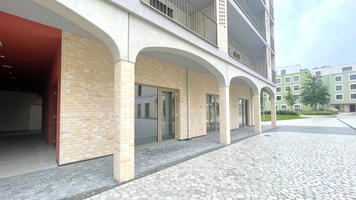 Eingangsbereich eines modernen Gebäudes mit Arkaden und heller Ziegelfassade.