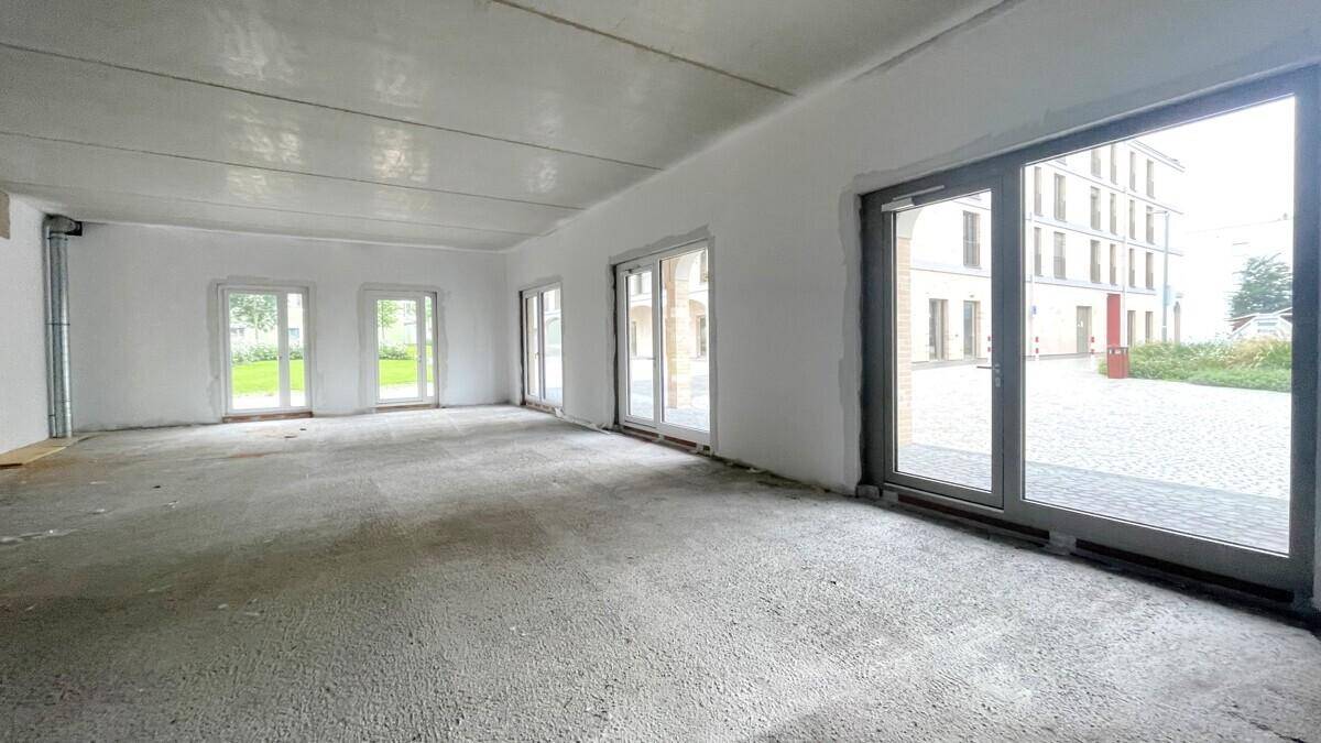 Großer, leerer Gewerberaum im Rohbauzustand mit vielen Fenstern und Blick nach draußen.