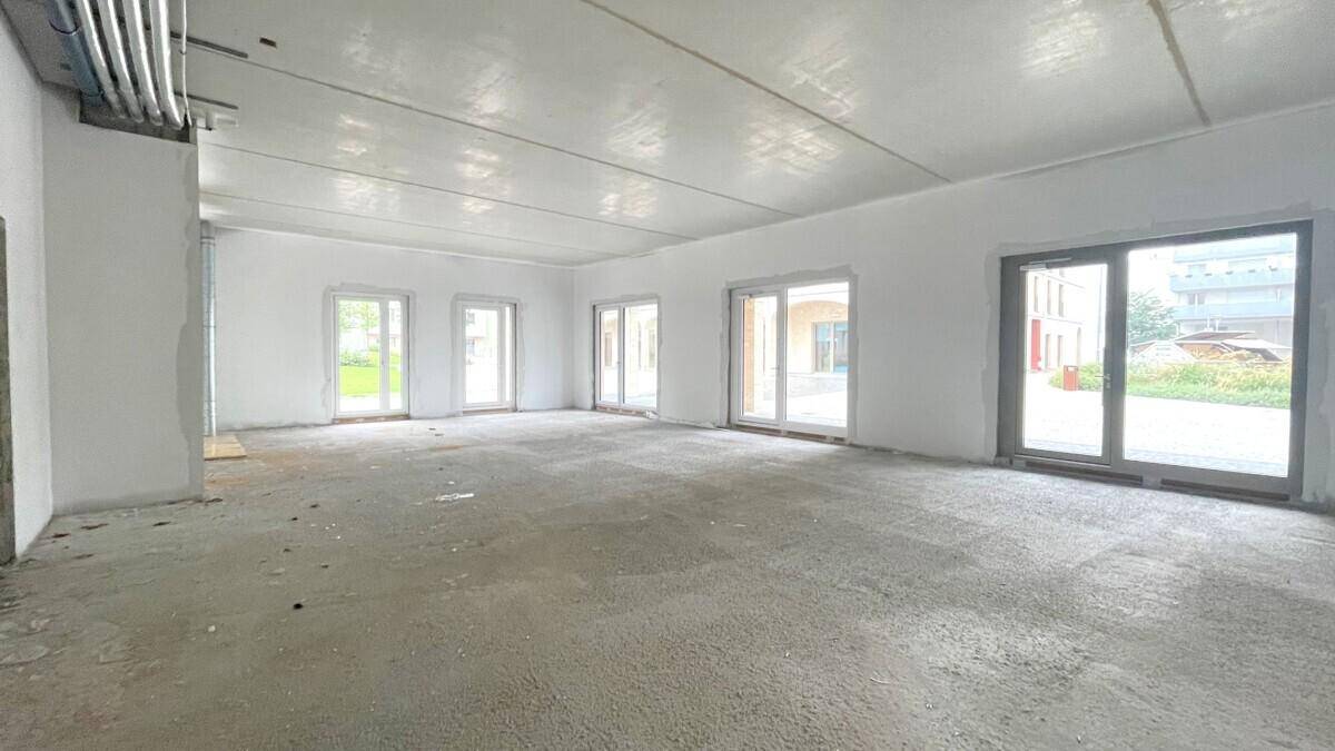 Weitläufiger Gewerberaum im Rohbau mit vielen Fenstern, die viel Tageslicht hereinlassen.