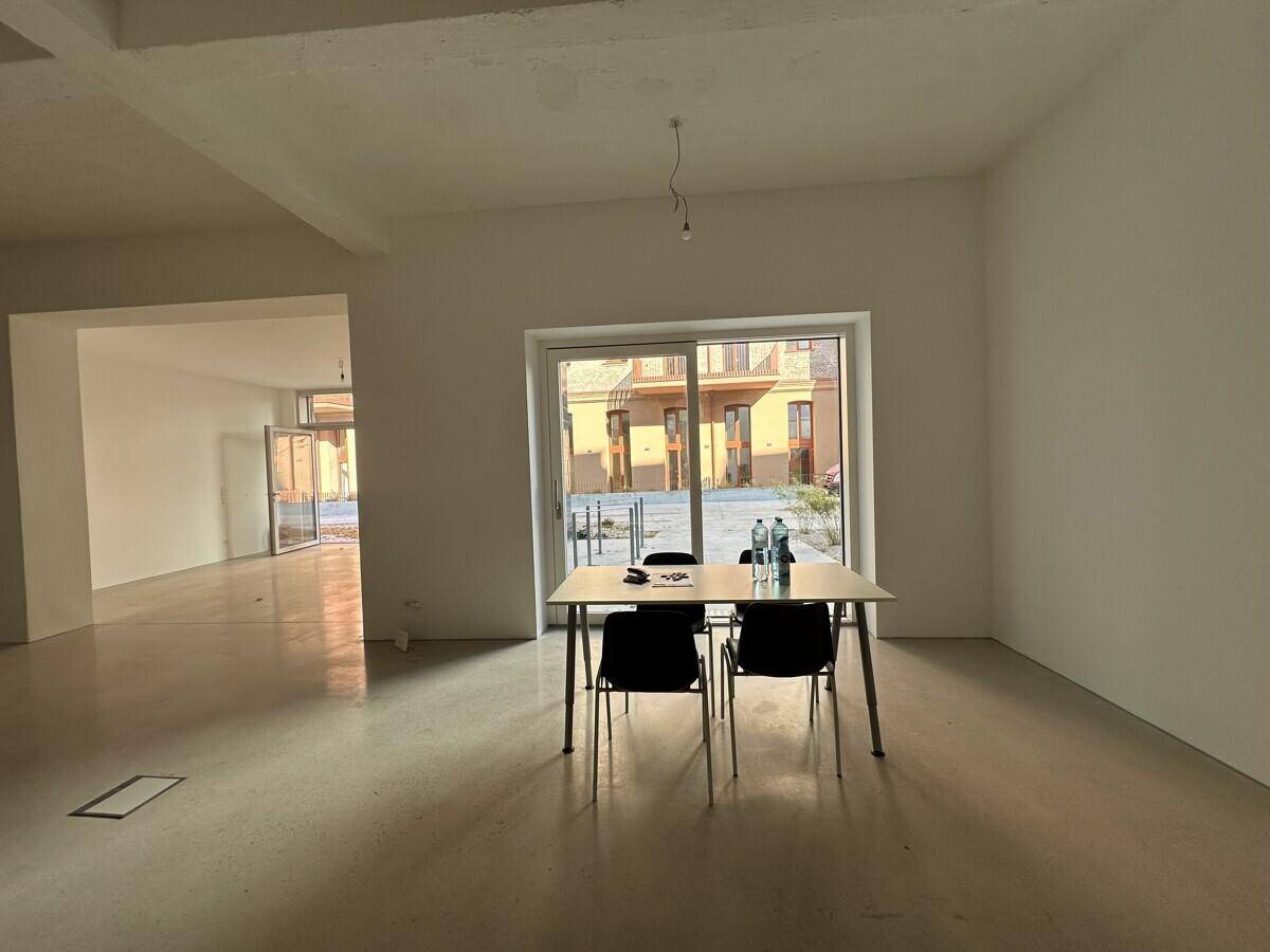 Heller Gewerberaum mit Betonboden und einem Tisch, der durch ein großes Fenster viel Tageslicht erhält.