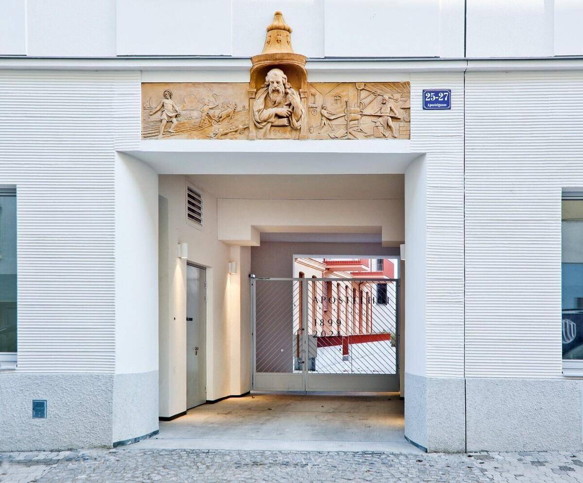 Eingangsbereich eines Gebäudes mit einem Torbogen, dekorativem Relief und Blick in den Innenhof.