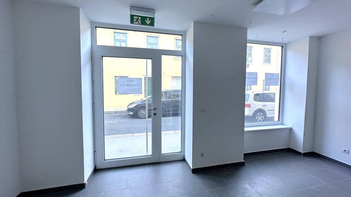 Innenansicht eines leeren Ladenlokals mit Eingangstür und großen Schaufenstern zur Straße.