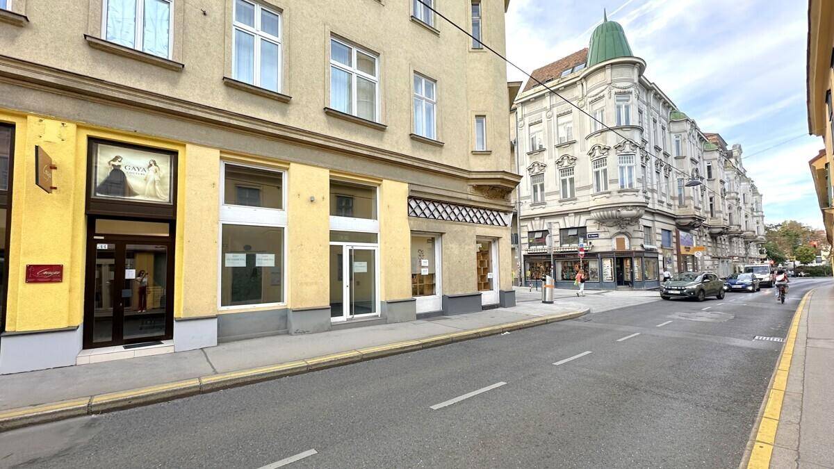 Straßenansicht mit dem Eckgebäude und angrenzenden historischen Bauten, belebte Straße mit parkenden Autos.