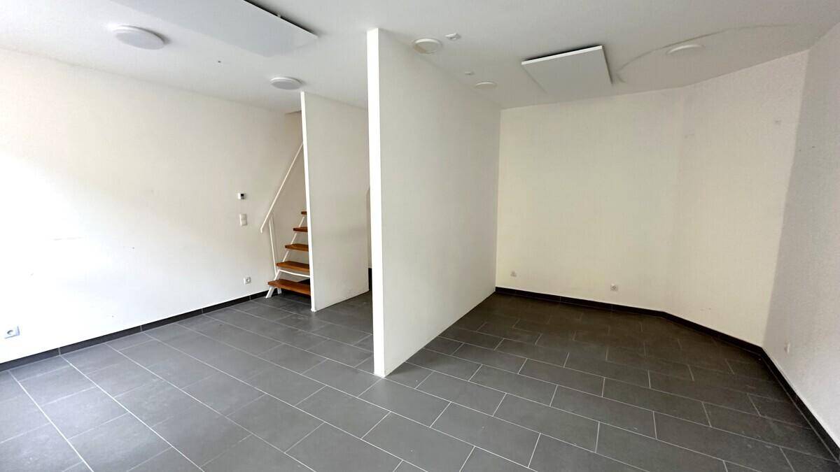 Geräumiger, leerer Geschäftsraum mit dunklem Fliesenboden und einer Holztreppe, die in eine obere Etage führt.