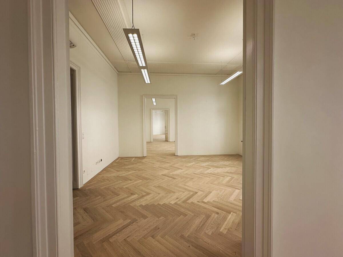 Langer Flur mit Fischgrätparkett und mehreren Türen, die zu weiteren Büroräumen führen.