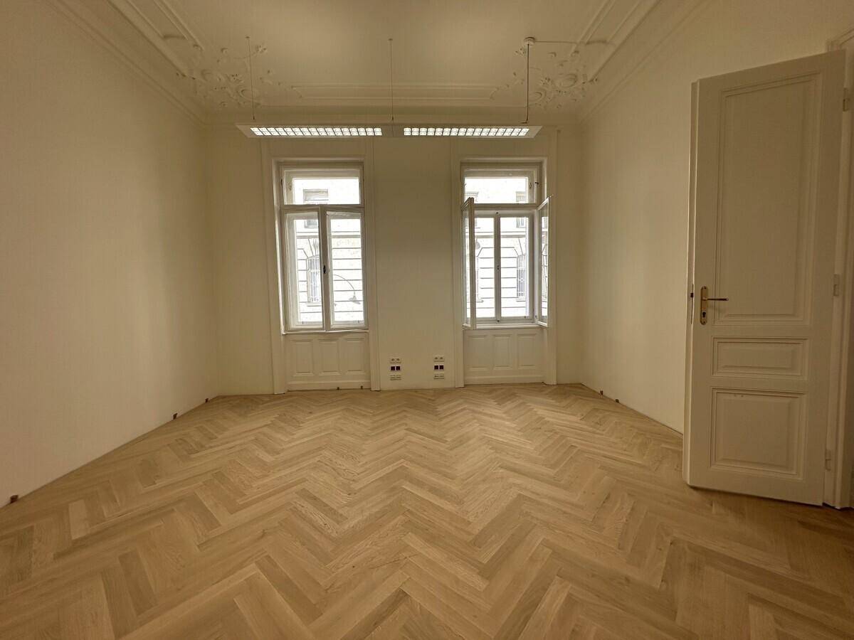 Helles Büro mit Fischgrätparkett, Stuckdecken und zwei hohen Fenstern, die den Raum erhellen.