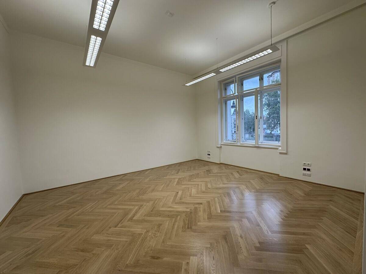 Eckbüro mit Fischgrätparkett, einer großen Fensterfront und modernen Deckenleuchten.