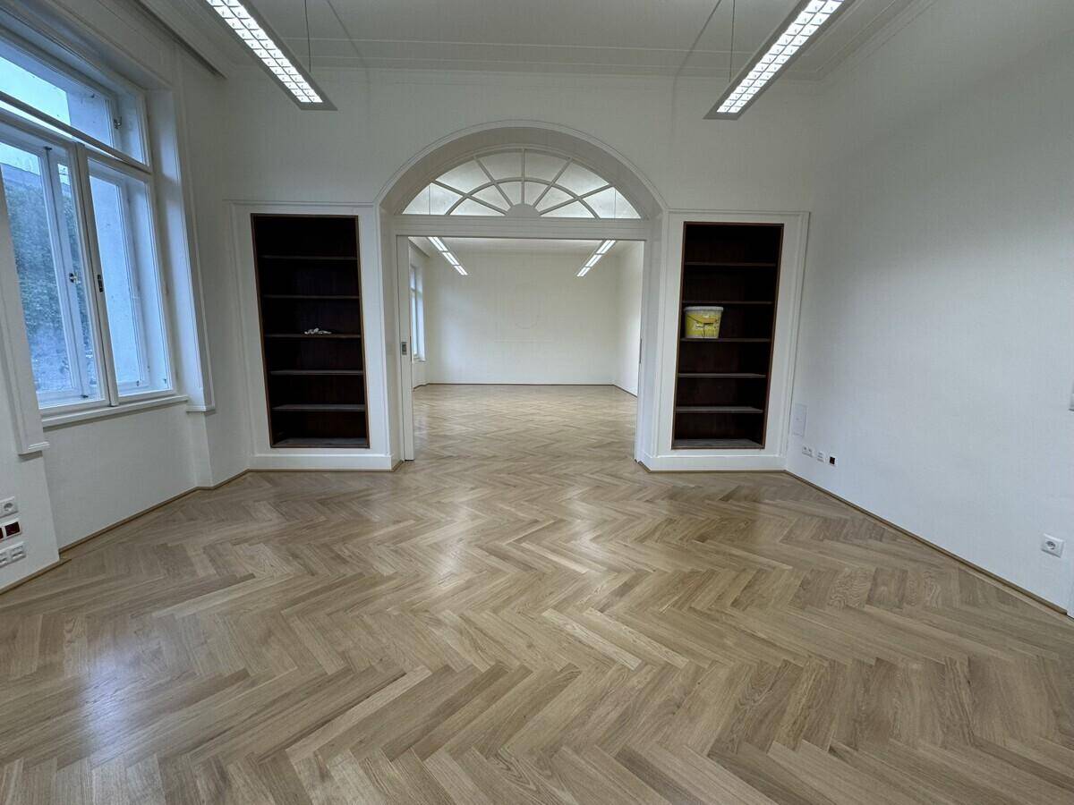 Großes Büro mit Fischgrätparkett, Einbauregalen und einer eleganten Doppeltür zu einem weiteren Raum.