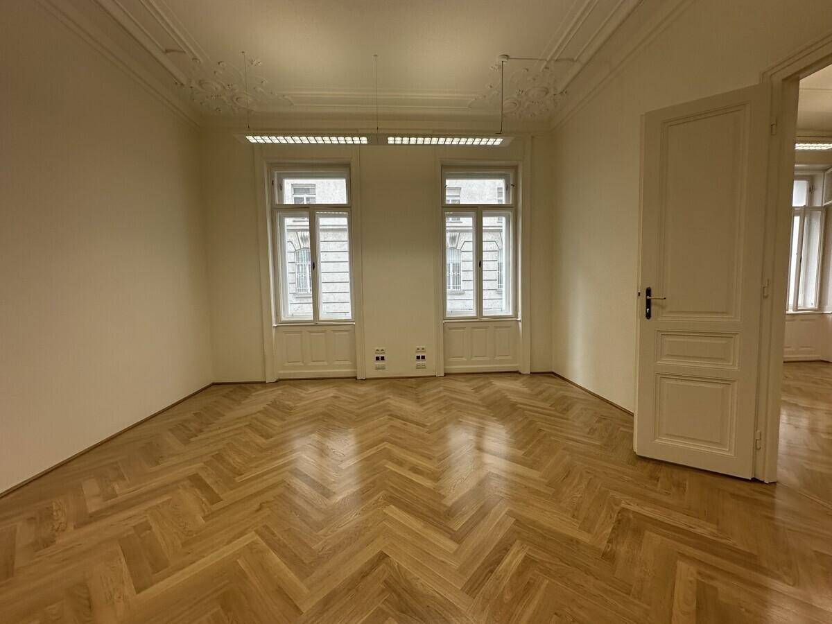 Helles Büro mit Fischgrätparkett, Stuckdecken und zwei hohen Fenstern, die den Raum erhellen.