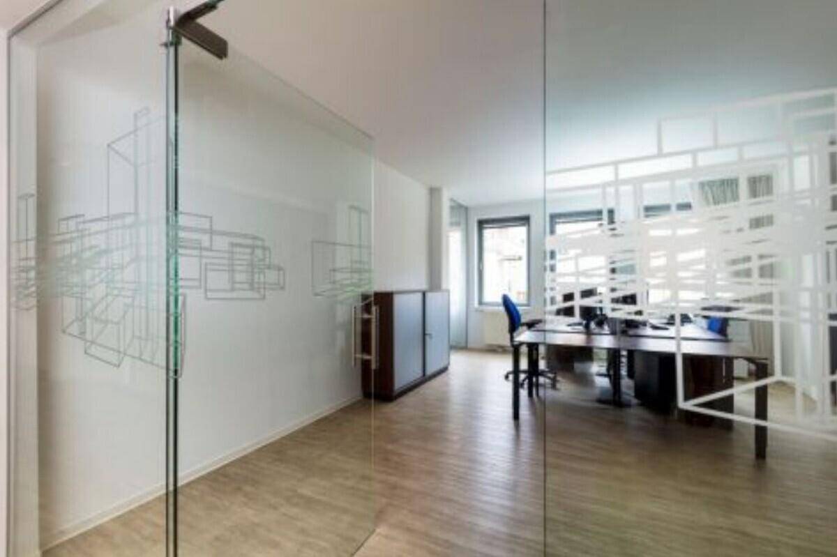 Modernes Büro mit Glaswänden, Schrank und mehreren Arbeitsplätzen.