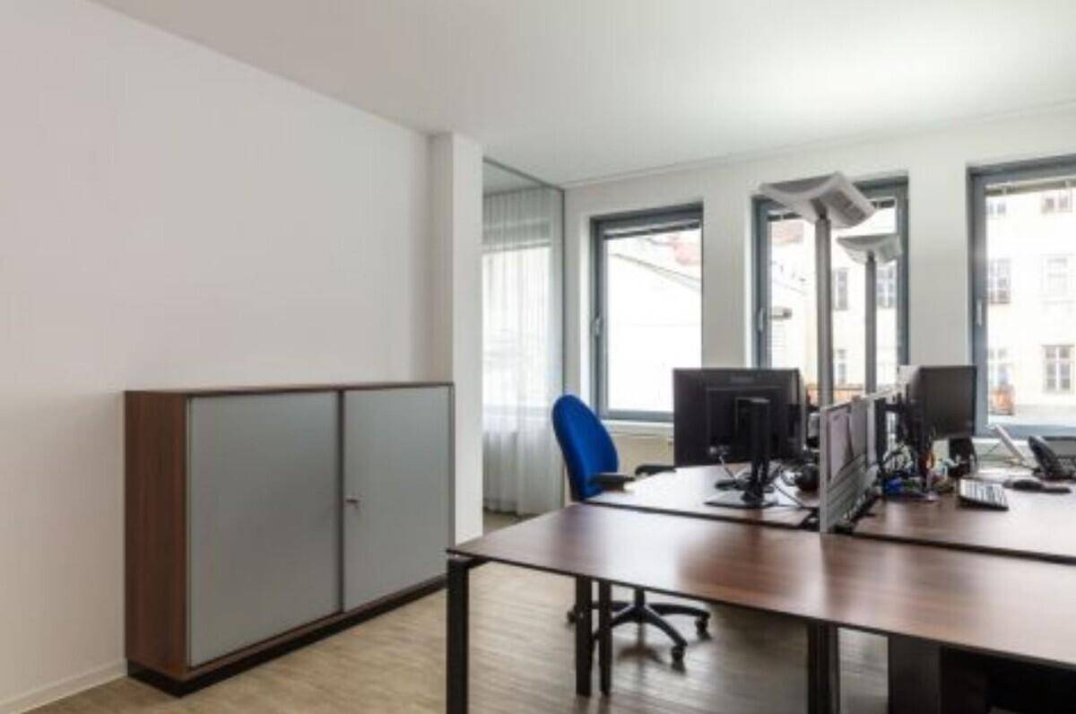 Heller Büroraum mit mehreren Arbeitsplätzen, Fenstern und einem Schrank.