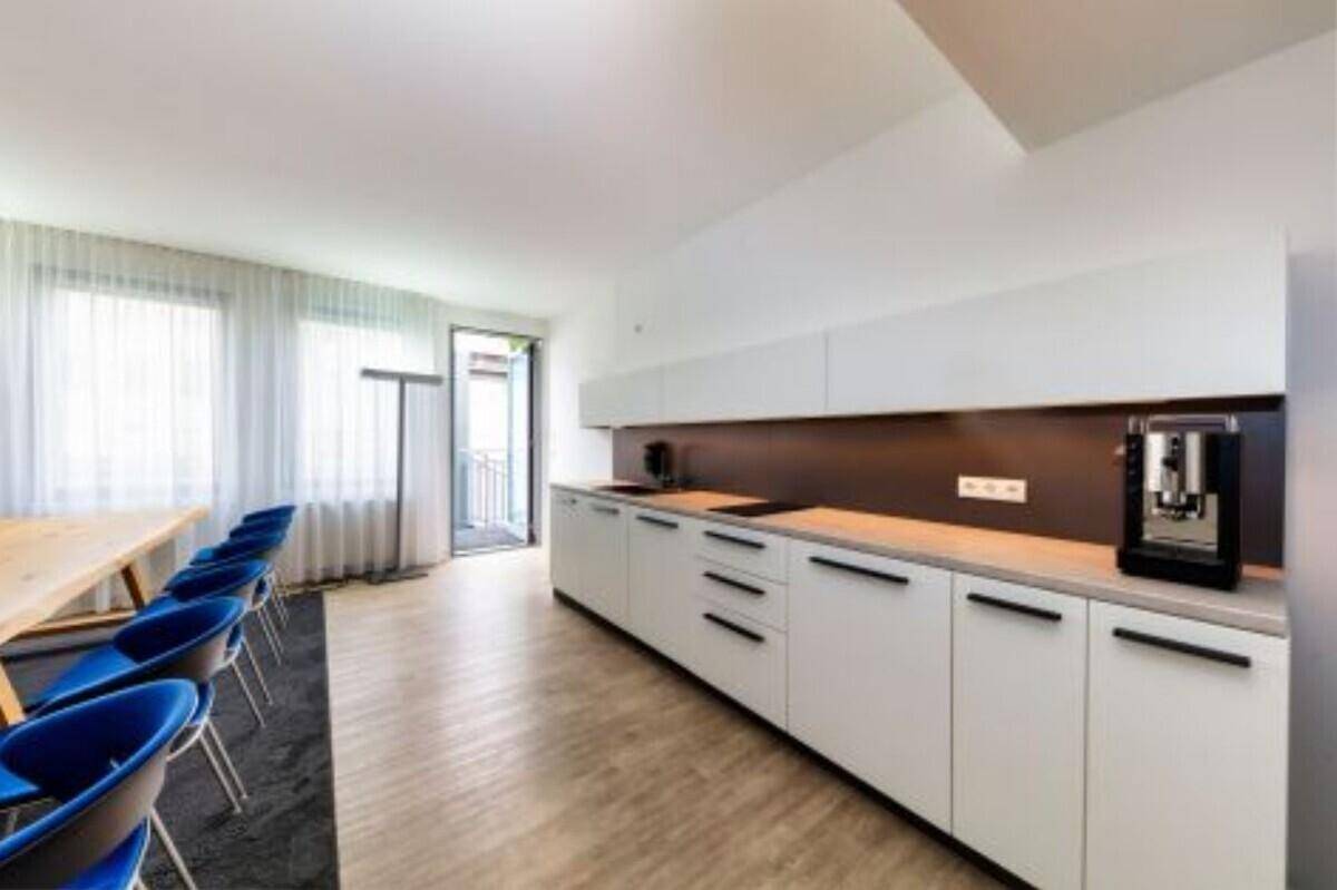 Helle Teeküche mit weißen Schränken, Kaffeemaschine und Zugang zu einem Balkon.