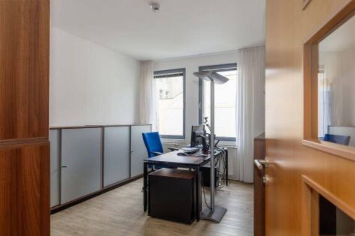 Einzelbüro mit Schreibtisch, Bürostuhl und Schränken, durch eine Holztür sichtbar.