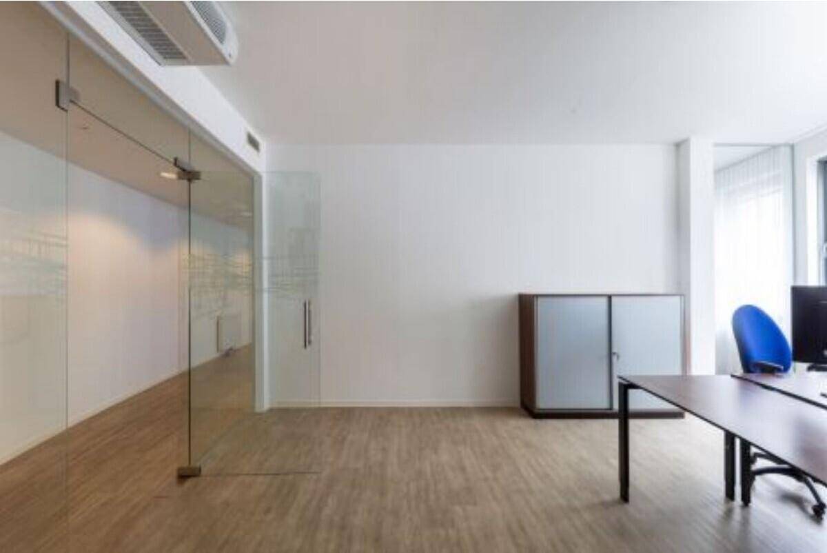 Geräumiges Büro mit Glaswand, Schrank und viel Platz für Arbeitsplätze.