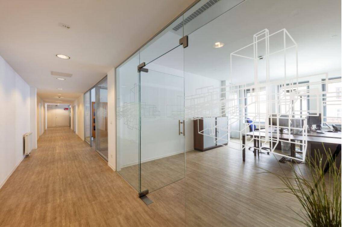 Moderner Bürogang mit Glaswänden und Blick in ein helles Büro.
